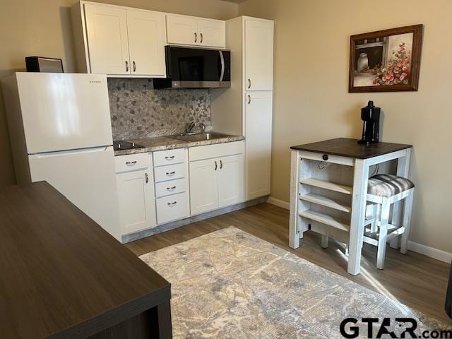 kitchen featuring a sink, stainless steel microwave, light wood-style flooring, and freestanding refrigerator