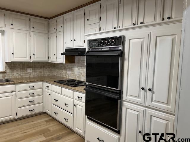 kitchen with white cabinets, backsplash, black appliances, and under cabinet range hood