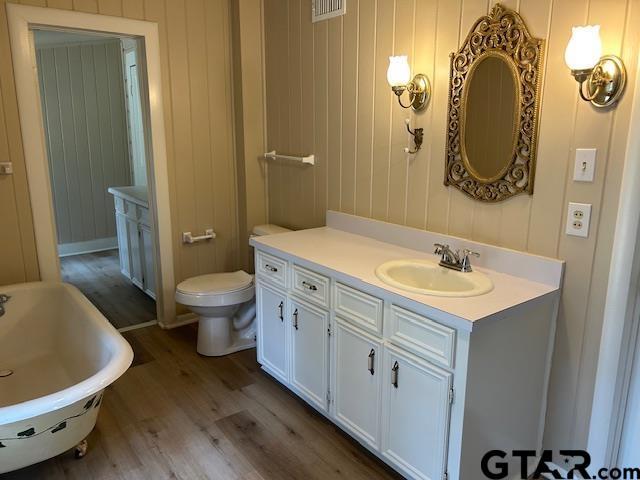 full bath with visible vents, a freestanding bath, wood finished floors, vanity, and toilet