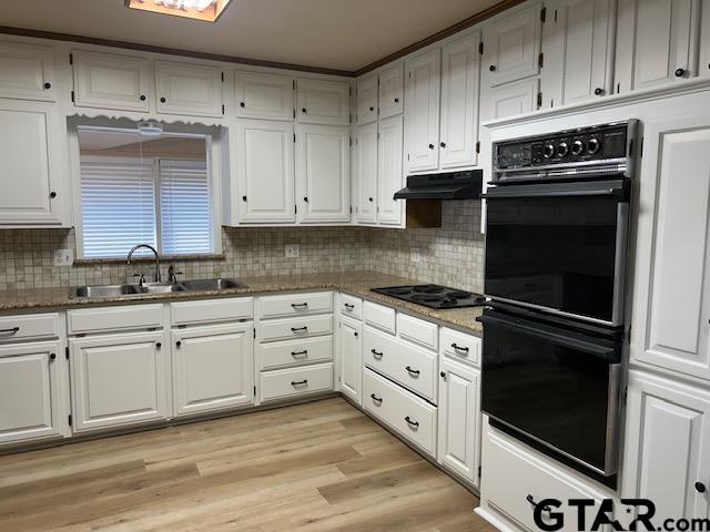 kitchen with white cabinetry, under cabinet range hood, a sink, backsplash, and black appliances