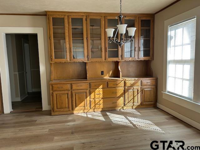 unfurnished dining area with an inviting chandelier, ornamental molding, plenty of natural light, and light wood-style flooring