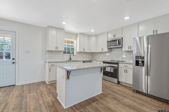 kitchen featuring sink, a center island, stainless steel appliances, light stone countertops, and white cabinets