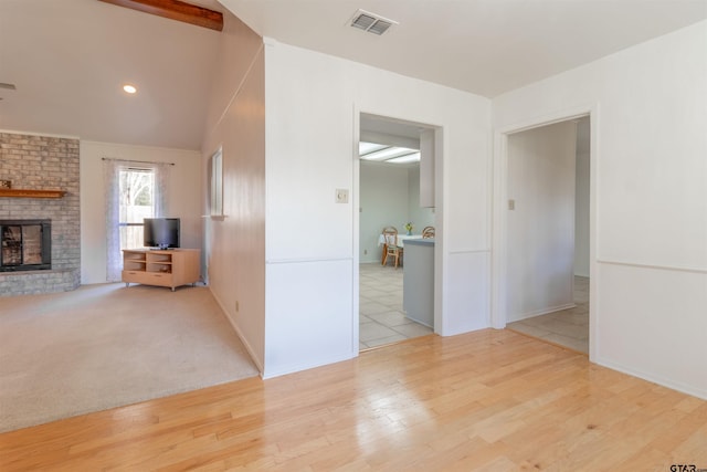 unfurnished living room featuring a brick fireplace, visible vents, vaulted ceiling, and wood finished floors