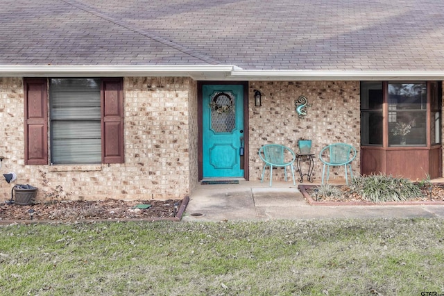 entrance to property featuring a shingled roof and brick siding