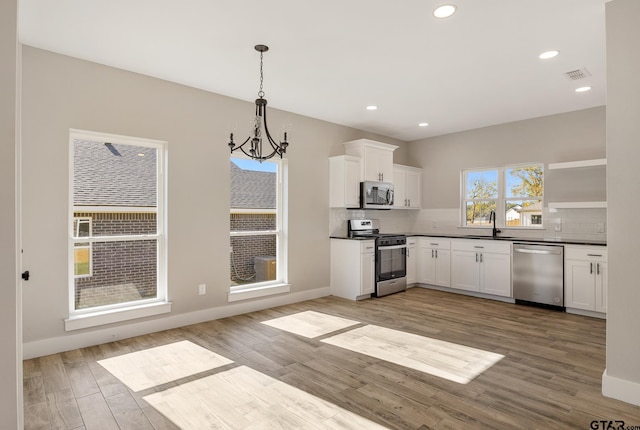 kitchen featuring white cabinetry, light wood-type flooring, stainless steel appliances, and pendant lighting