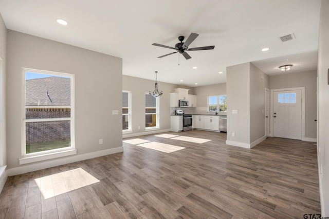 unfurnished living room with ceiling fan with notable chandelier and light hardwood / wood-style flooring