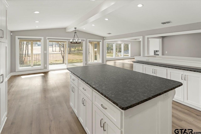 kitchen featuring white cabinetry, vaulted ceiling with beams, a center island, dark stone counters, and light wood-type flooring