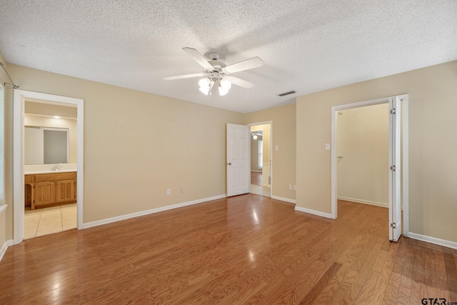 unfurnished bedroom with sink, ceiling fan, ensuite bathroom, a textured ceiling, and light wood-type flooring