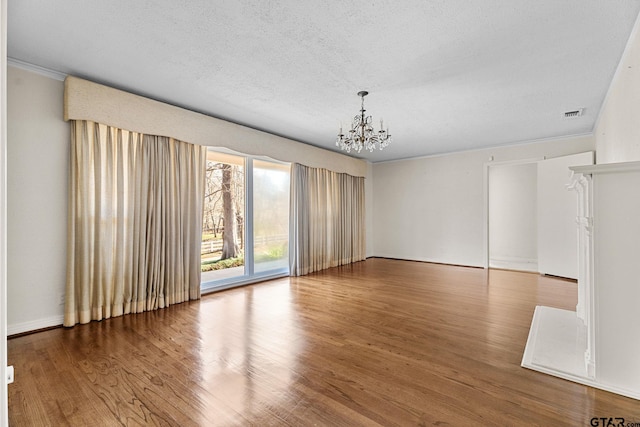 spare room with an inviting chandelier, hardwood / wood-style flooring, ornamental molding, and a textured ceiling