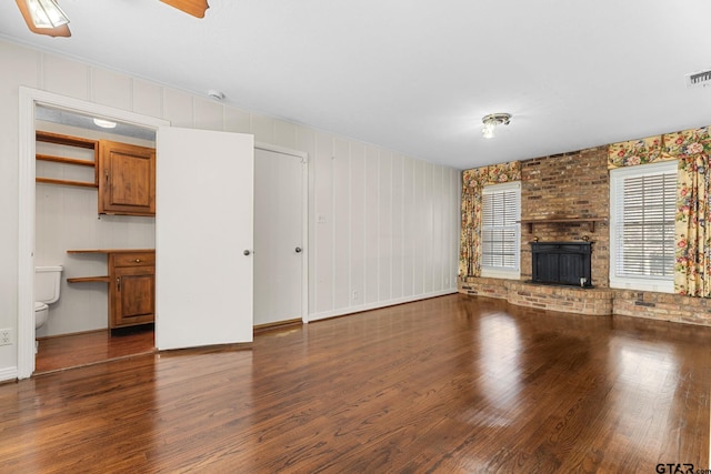 unfurnished living room featuring brick wall, a brick fireplace, dark wood-type flooring, and built in desk