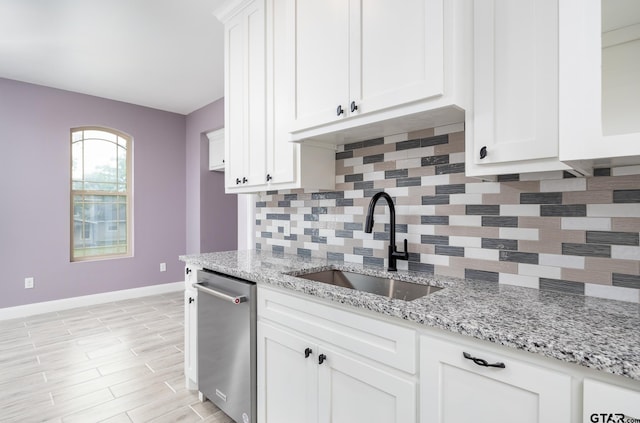 kitchen featuring dishwasher, white cabinets, sink, tasteful backsplash, and light stone counters