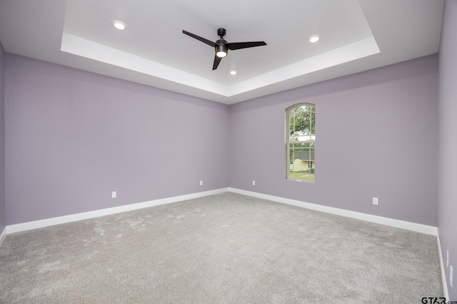 spare room with ceiling fan, carpet floors, and a tray ceiling