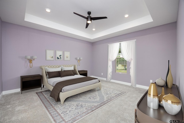 bedroom with ceiling fan, light colored carpet, and a tray ceiling