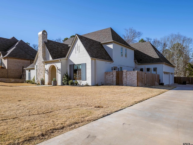 french provincial home with an attached garage, fence, concrete driveway, stucco siding, and a chimney