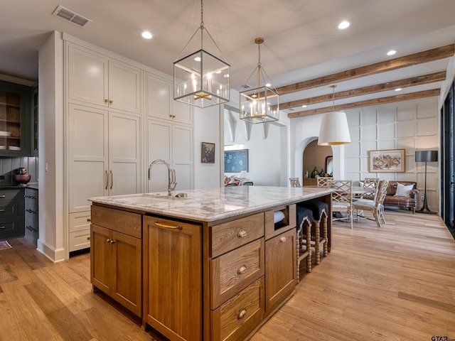 kitchen with light stone counters, arched walkways, brown cabinets, a sink, and light wood-type flooring