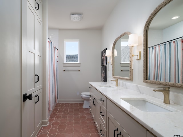 bathroom featuring double vanity, a sink, toilet, and baseboards