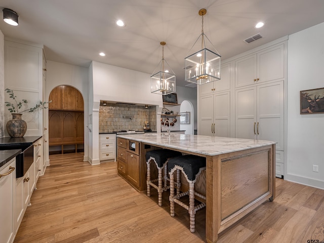 kitchen with tasteful backsplash, arched walkways, light wood-style flooring, and recessed lighting