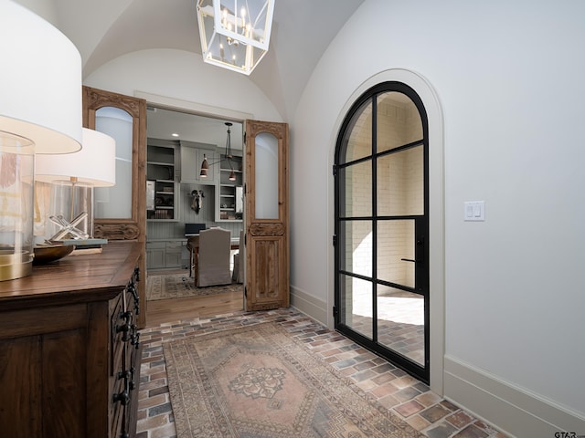 interior space featuring lofted ceiling, brick floor, baseboards, and a chandelier