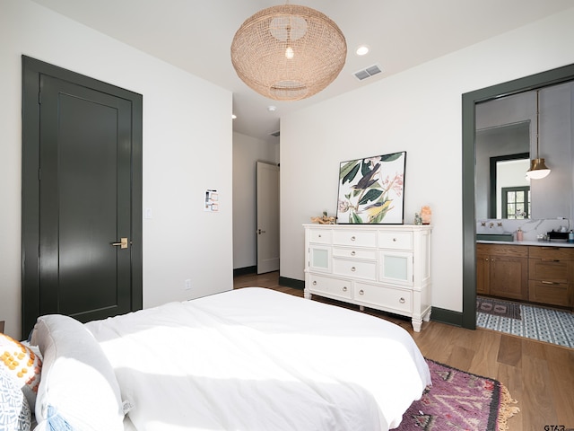 bedroom with ensuite bath, wood finished floors, visible vents, and recessed lighting