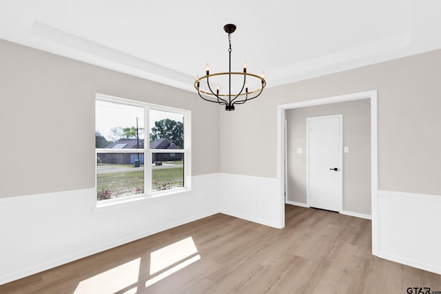 empty room featuring a wainscoted wall, a notable chandelier, a tray ceiling, and wood finished floors