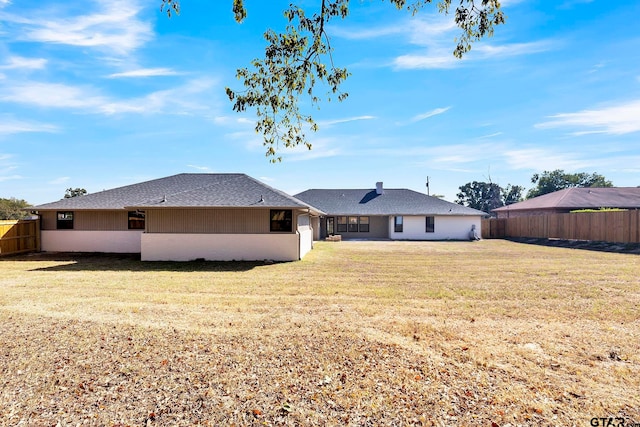 rear view of property featuring a lawn and fence