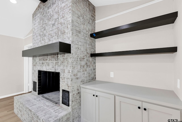 living area featuring visible vents, crown molding, a fireplace, lofted ceiling, and light wood-type flooring