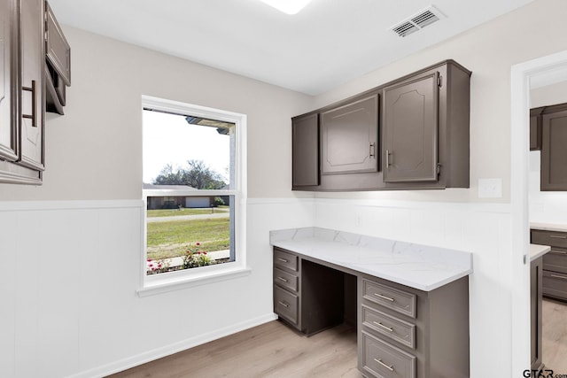 office featuring built in desk, light wood-style flooring, visible vents, and a wainscoted wall