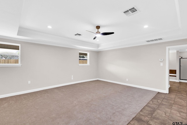 carpeted empty room with a tray ceiling, visible vents, and a ceiling fan