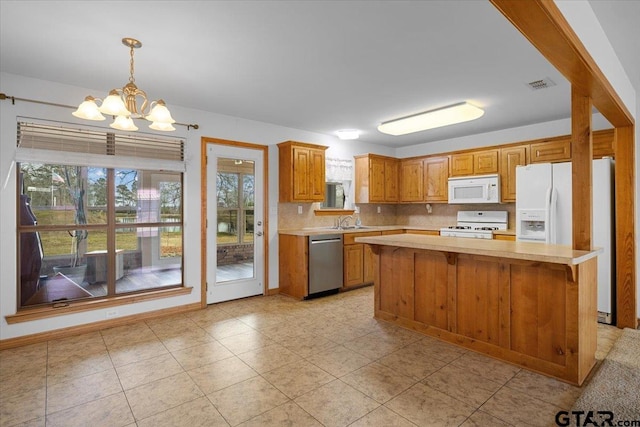 kitchen with sink, hanging light fixtures, a kitchen island, white appliances, and backsplash