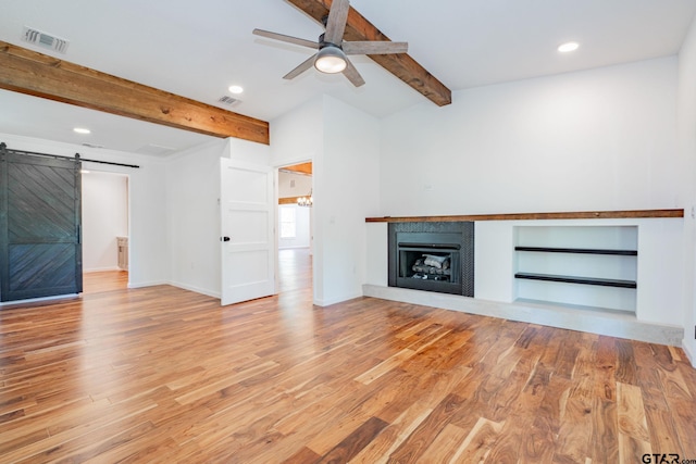 unfurnished living room featuring built in shelves, light hardwood / wood-style flooring, a barn door, and beam ceiling