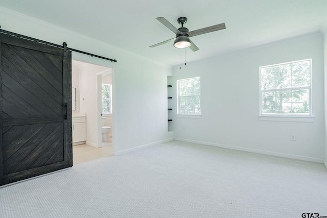 carpeted spare room featuring ornamental molding, ceiling fan, and a barn door