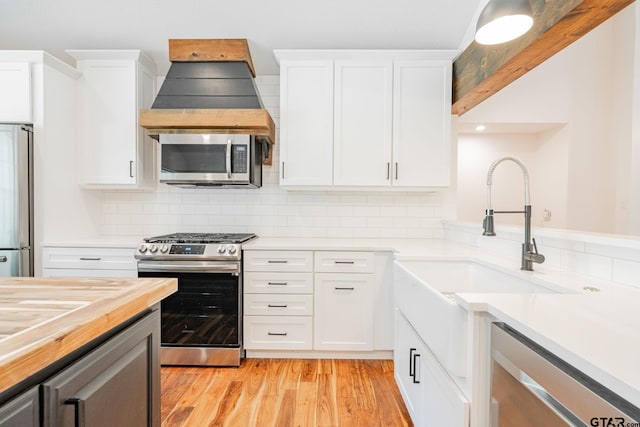 kitchen featuring white cabinets, backsplash, appliances with stainless steel finishes, and light hardwood / wood-style flooring