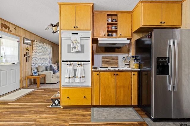 10929 County Road 41, Tyler, TX 75706 - kitchen featuring stainless steel refrigerator with ice dispenser, white double oven, under cabinet range hood, wood finished floors, and wooden walls