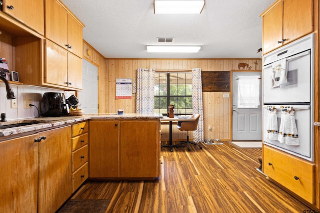 10929 County Road 41, Tyler, TX 75706 - kitchen featuring white double oven, wood walls, dark wood-style floors, a peninsula, and a textured ceiling