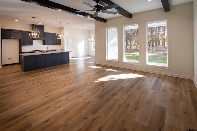 unfurnished living room with beamed ceiling, wood-type flooring, ceiling fan, and sink