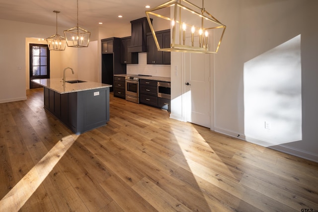 kitchen with decorative backsplash, sink, stainless steel stove, hanging light fixtures, and an island with sink