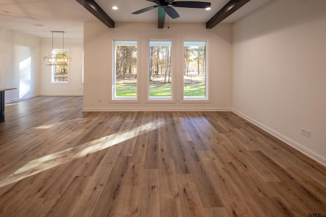 empty room with hardwood / wood-style flooring, ceiling fan with notable chandelier, and beam ceiling