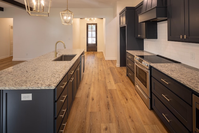 kitchen with custom exhaust hood, hanging light fixtures, sink, an island with sink, and stainless steel range