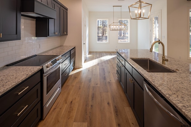 kitchen with light stone countertops, appliances with stainless steel finishes, sink, decorative light fixtures, and light hardwood / wood-style floors