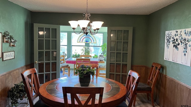 dining area featuring a notable chandelier, wooden walls, and a textured ceiling