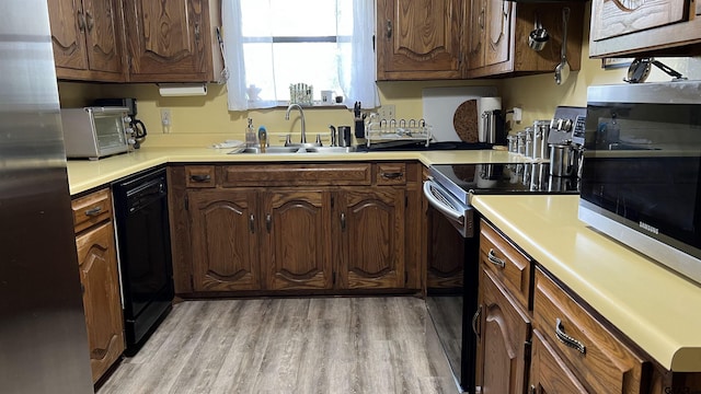 kitchen with black dishwasher, sink, stainless steel fridge, light hardwood / wood-style floors, and electric stove