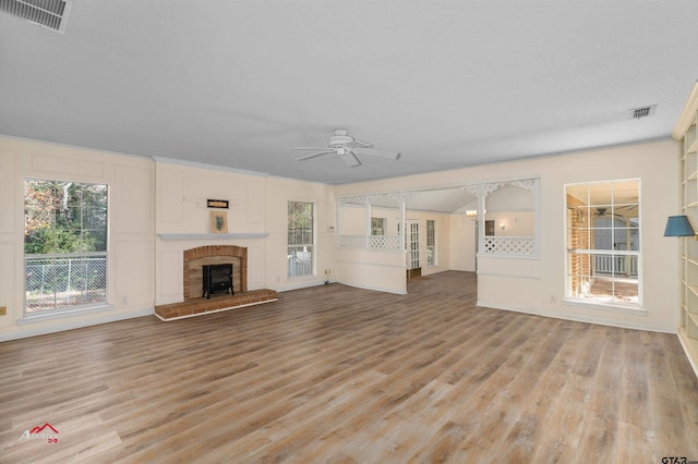 unfurnished living room with a brick fireplace, light wood-type flooring, ceiling fan, and a textured ceiling