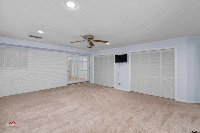 unfurnished bedroom with light colored carpet, ceiling fan, a textured ceiling, and multiple closets