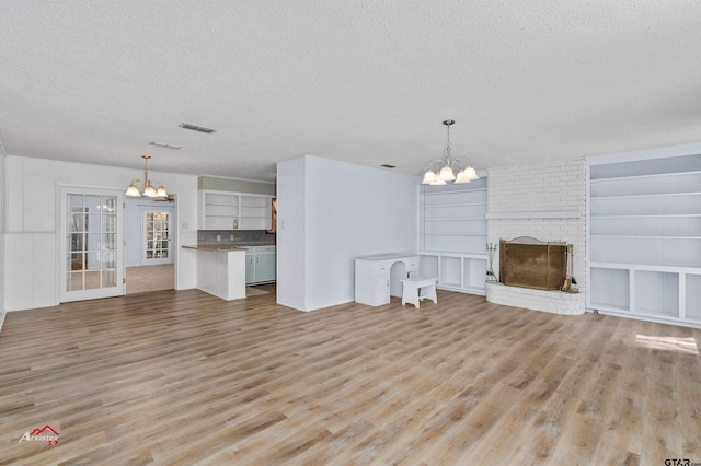 unfurnished living room featuring a textured ceiling, light hardwood / wood-style floors, a chandelier, and a fireplace