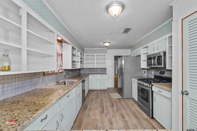 kitchen with stainless steel appliances, light stone countertops, white cabinetry, and sink