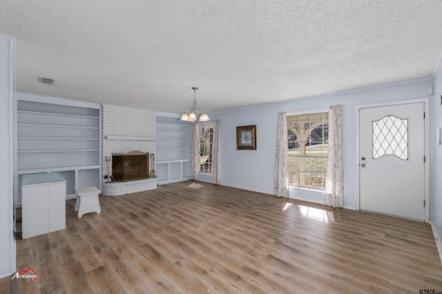 unfurnished living room featuring a brick fireplace, a textured ceiling, hardwood / wood-style flooring, and built in features