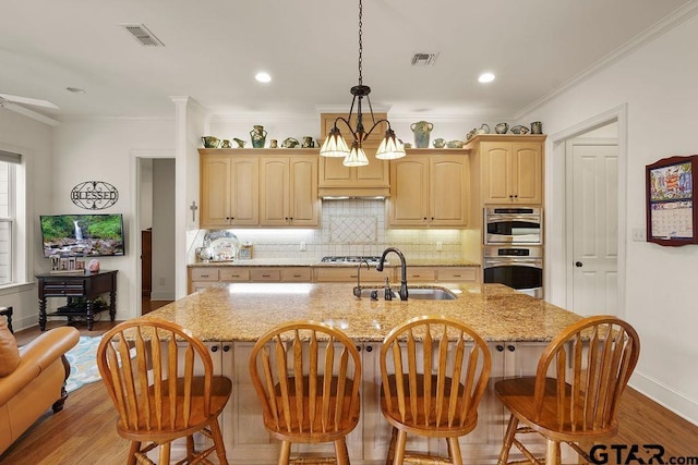 4007 Spartanburg Ln, Tyler, TX 75701 - kitchen featuring a sink, tasteful backsplash, a center island with sink, under cabinet range hood, and light stone countertops
