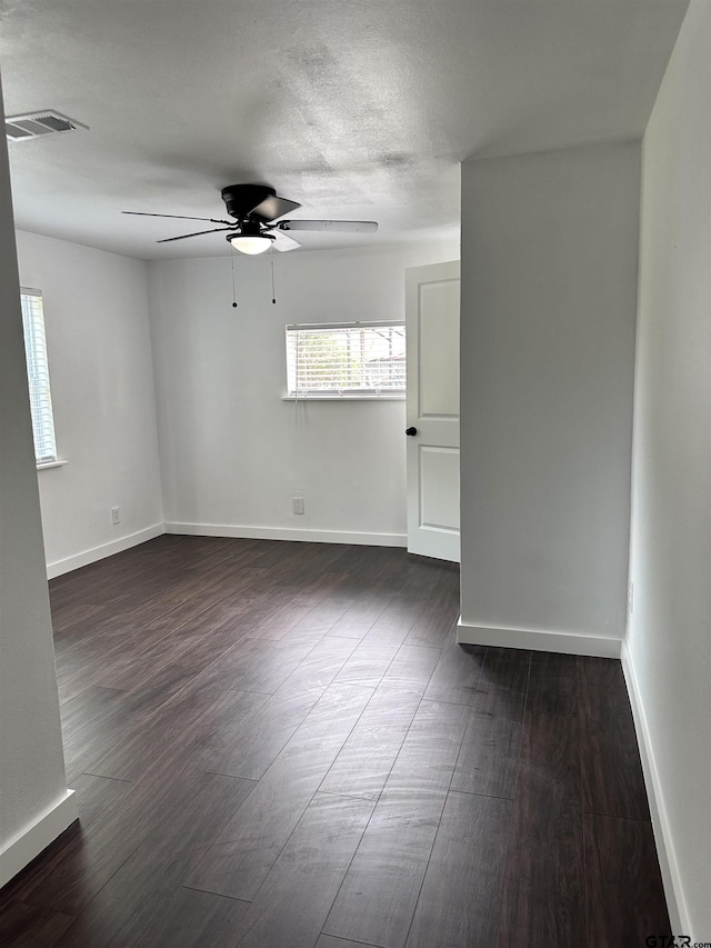 unfurnished room featuring dark wood-style floors, ceiling fan, visible vents, and baseboards