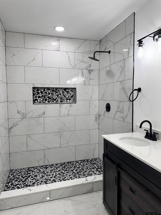 full bath featuring marble finish floor, a tile shower, and vanity