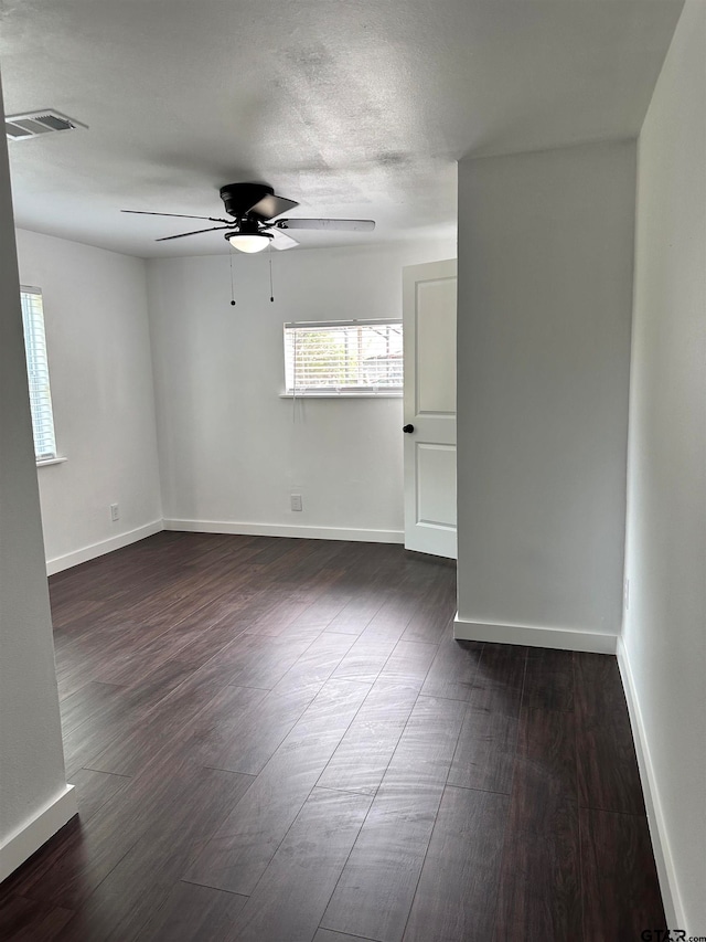 spare room with ceiling fan, visible vents, baseboards, and dark wood finished floors